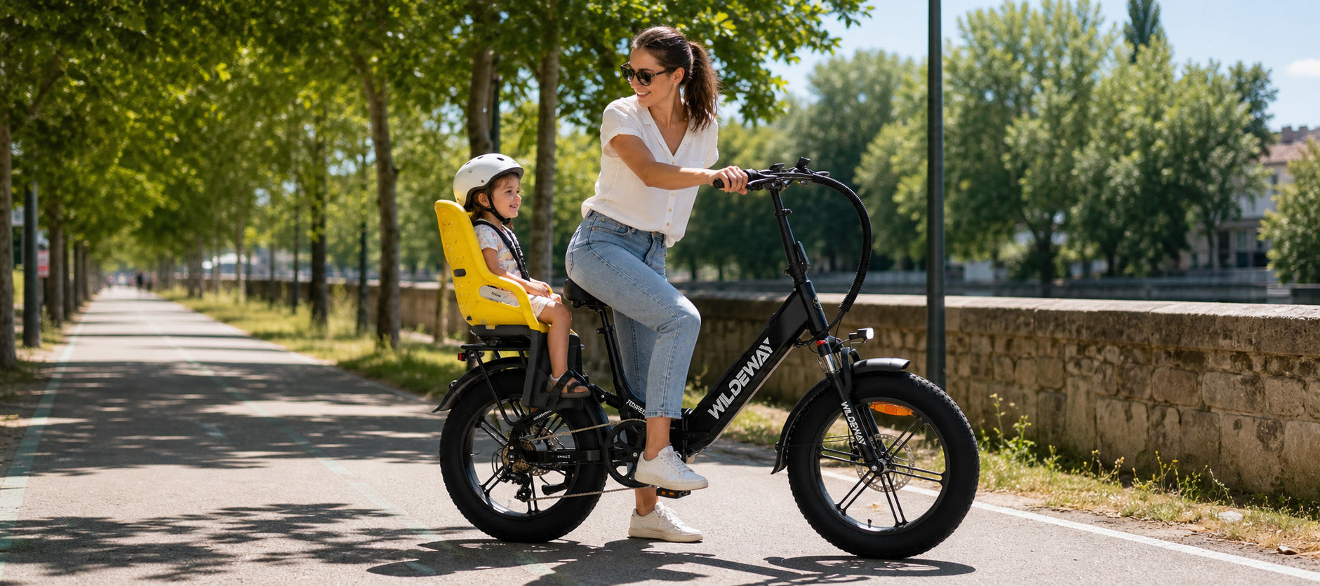 A happy parent safely riding a black WILDEWAY Torpedo step-through e-bike with a smiling child securely strapped into a rear child seat on a sunny summer day.