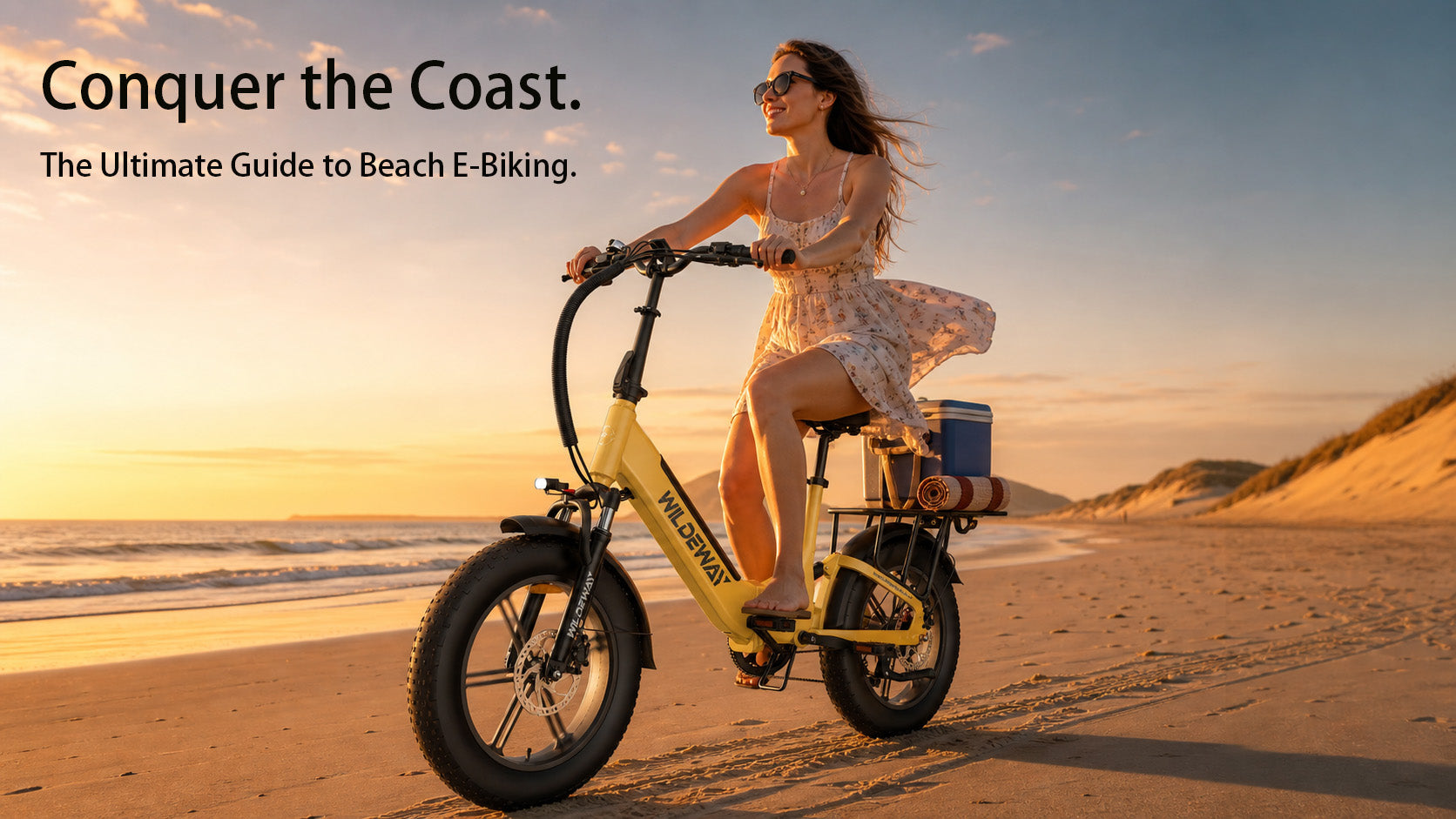 A person riding a Yellow WILDEWAY Torpedo fat tire e-bike on a sunny beach, leaving wide tire tracks in the wet sand.