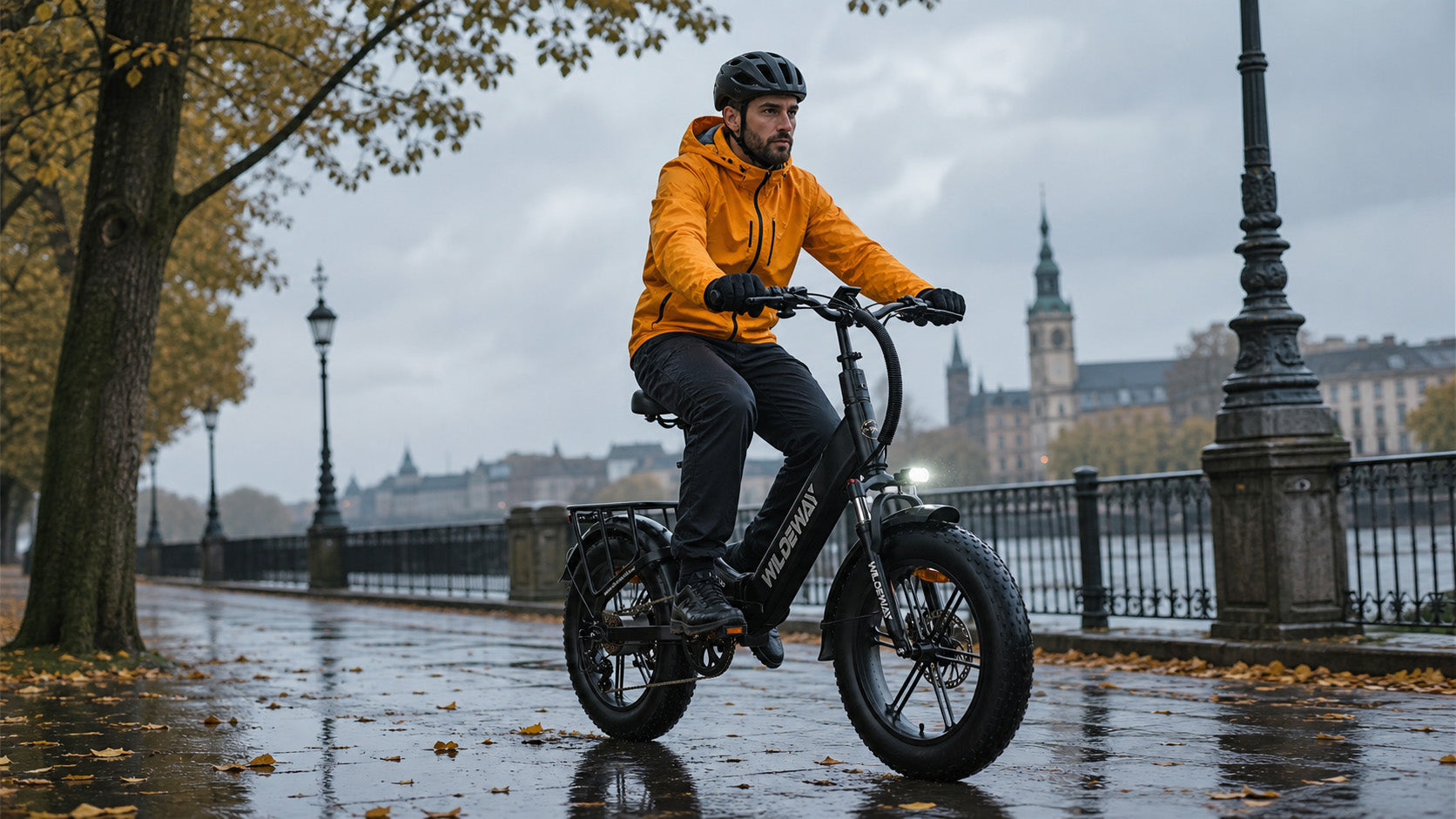 A cyclist wearing a bright yellow rain jacket riding a black WILDEWAY Torpedo fat tire e-bike on a wet autumn street covered in fallen leaves.
